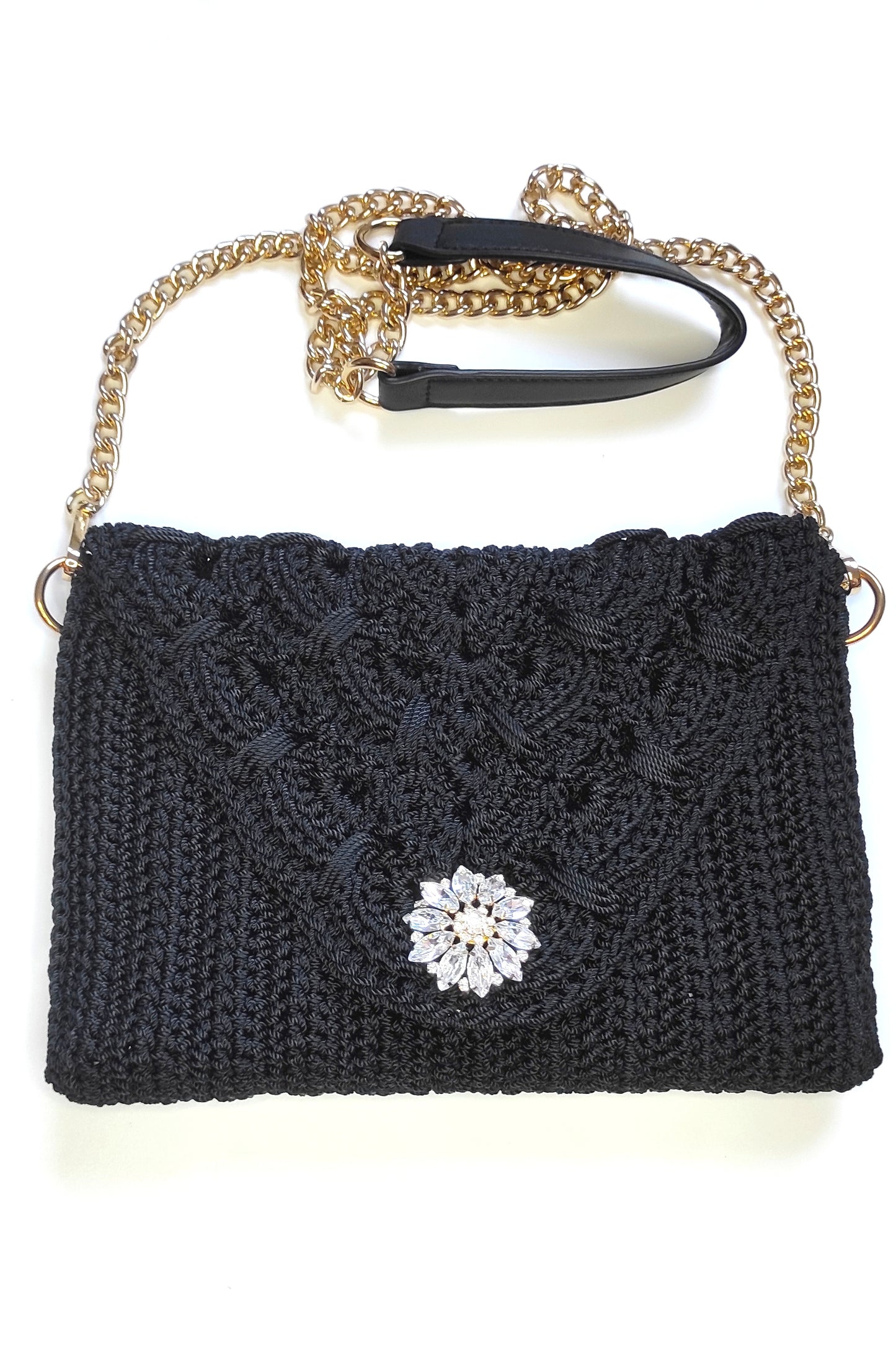 Bolso negro de fiesta estilo bandolera con aplique decorativo de pedrería acrílica en forma floral.