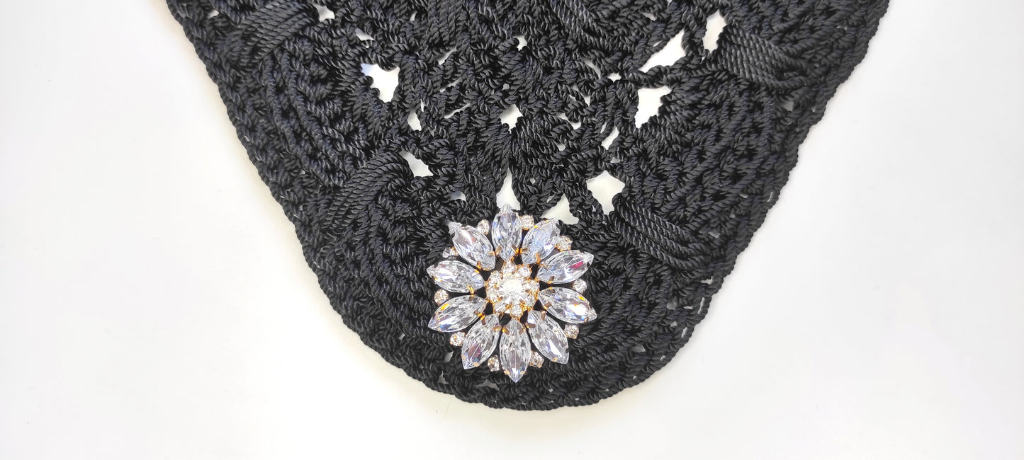 Bolso negro de fiesta estilo bandolera con aplique decorativo de pedrería acrílica en forma floral.