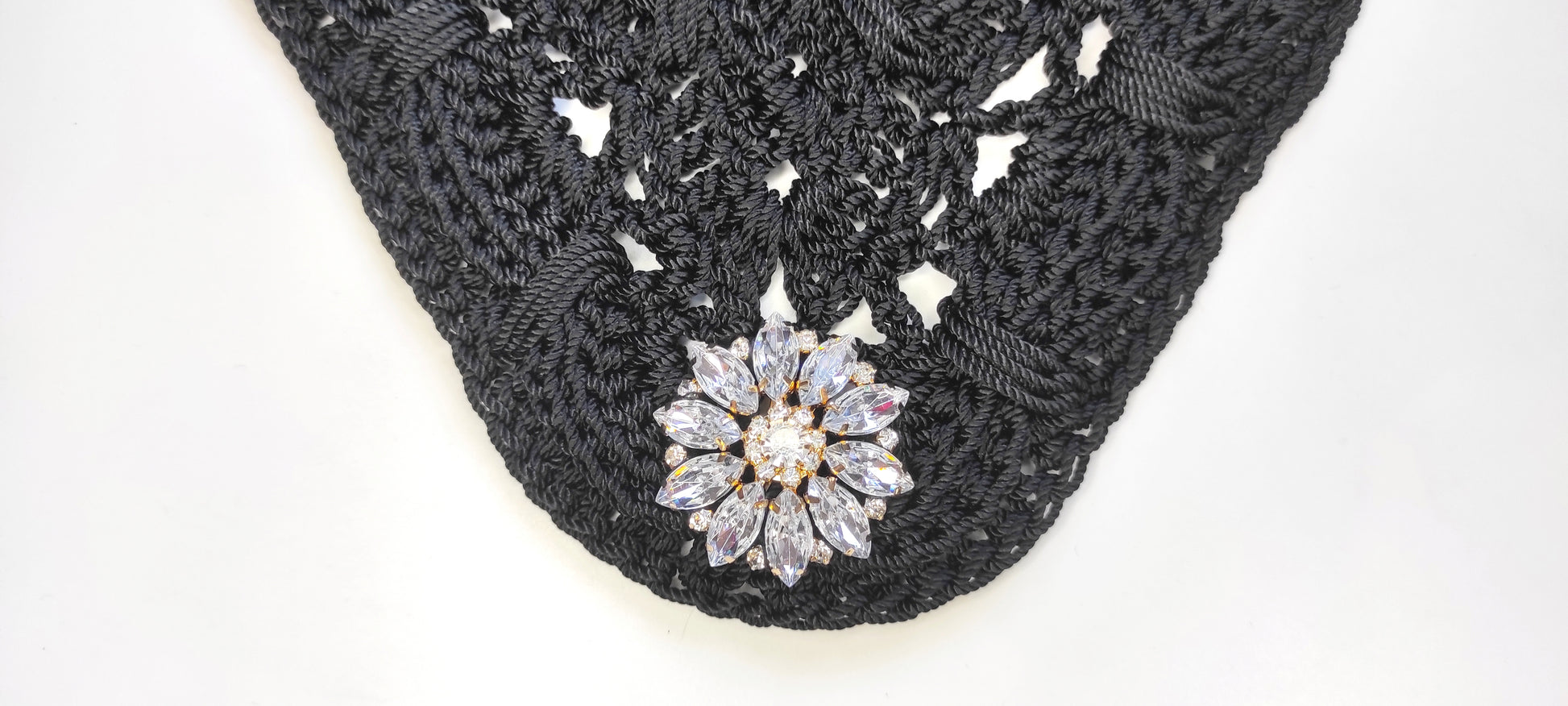 Bolso negro de fiesta estilo bandolera con aplique decorativo de pedrería acrílica en forma floral.